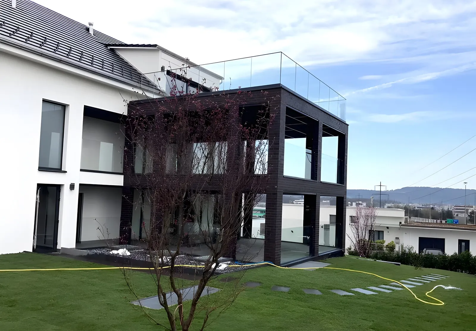 Neubau mit dunklem Anbau, grossen Fensterfronten und rahmenlosem Glasgeländer auf der Dachterrasse