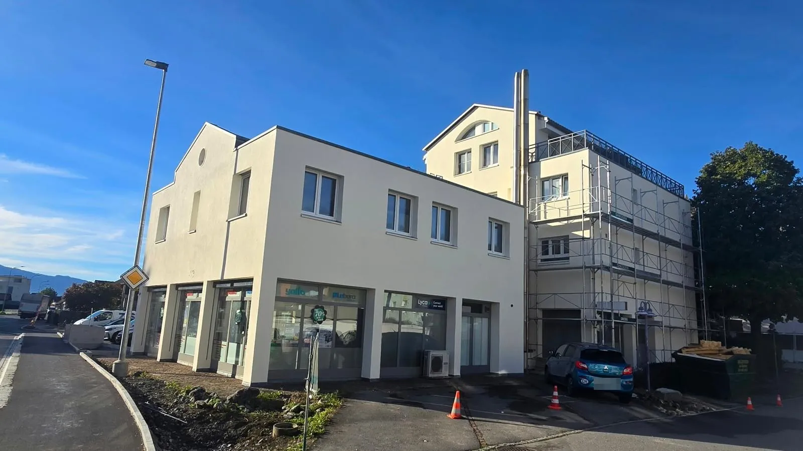 Renoviertes Wohn- und Geschäftshaus mit heller Fassade und neuen Fenstern, rechts noch eingerüstet
