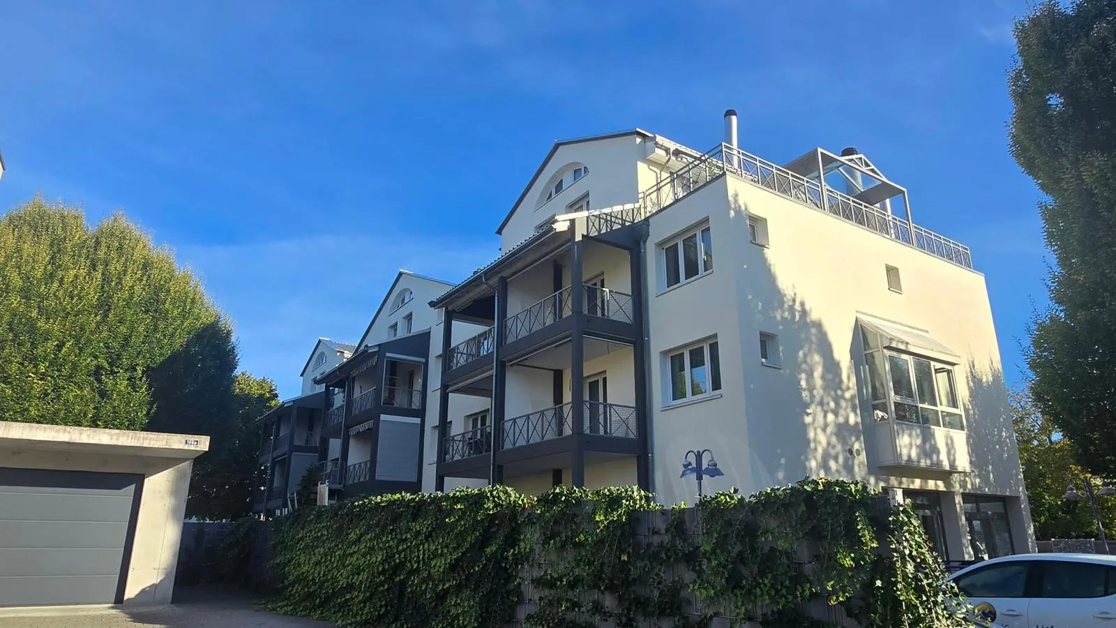 Mehrfamilienhaus mit heller Fassade, dunklen Balkonen und Dachterrasse mit Metallgeländer