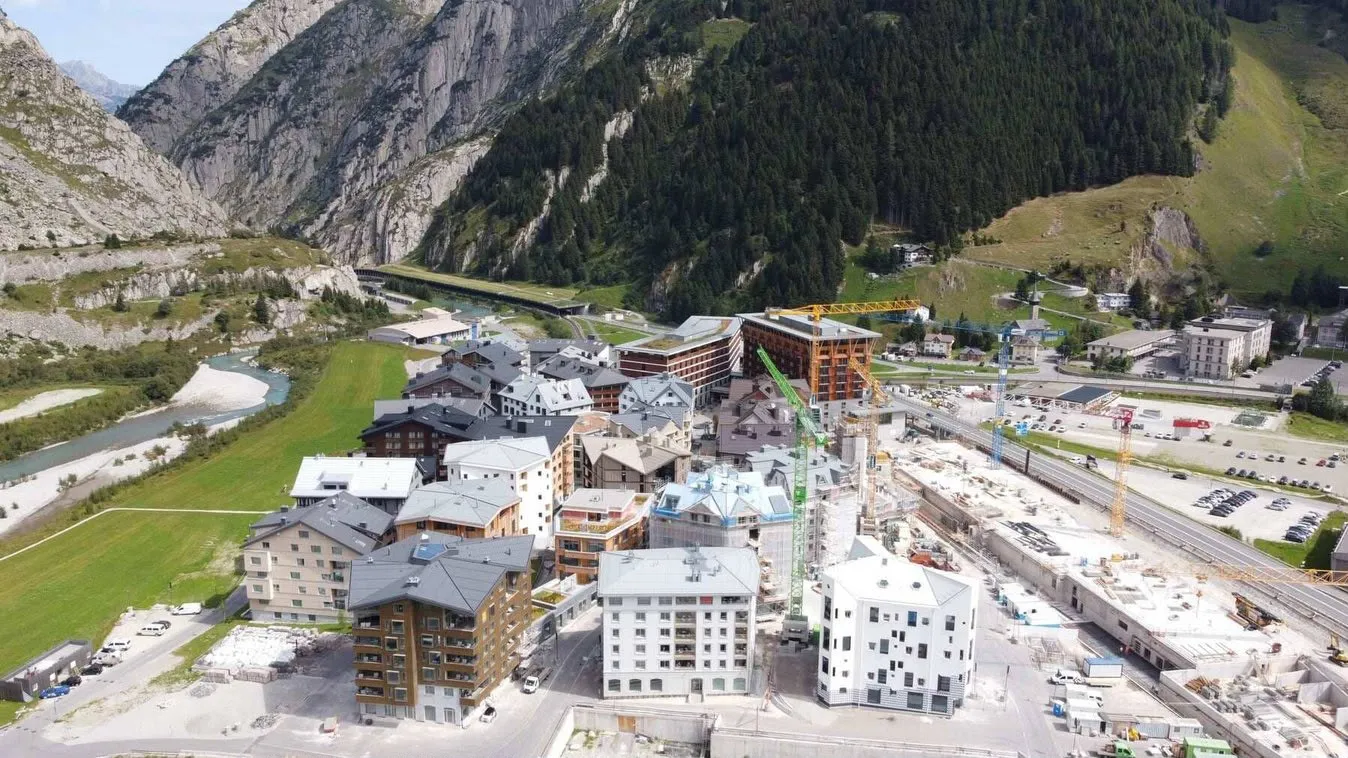 Luftaufnahme einer Überbauung in einem Bergdorf mit Neubauten und Baukränen